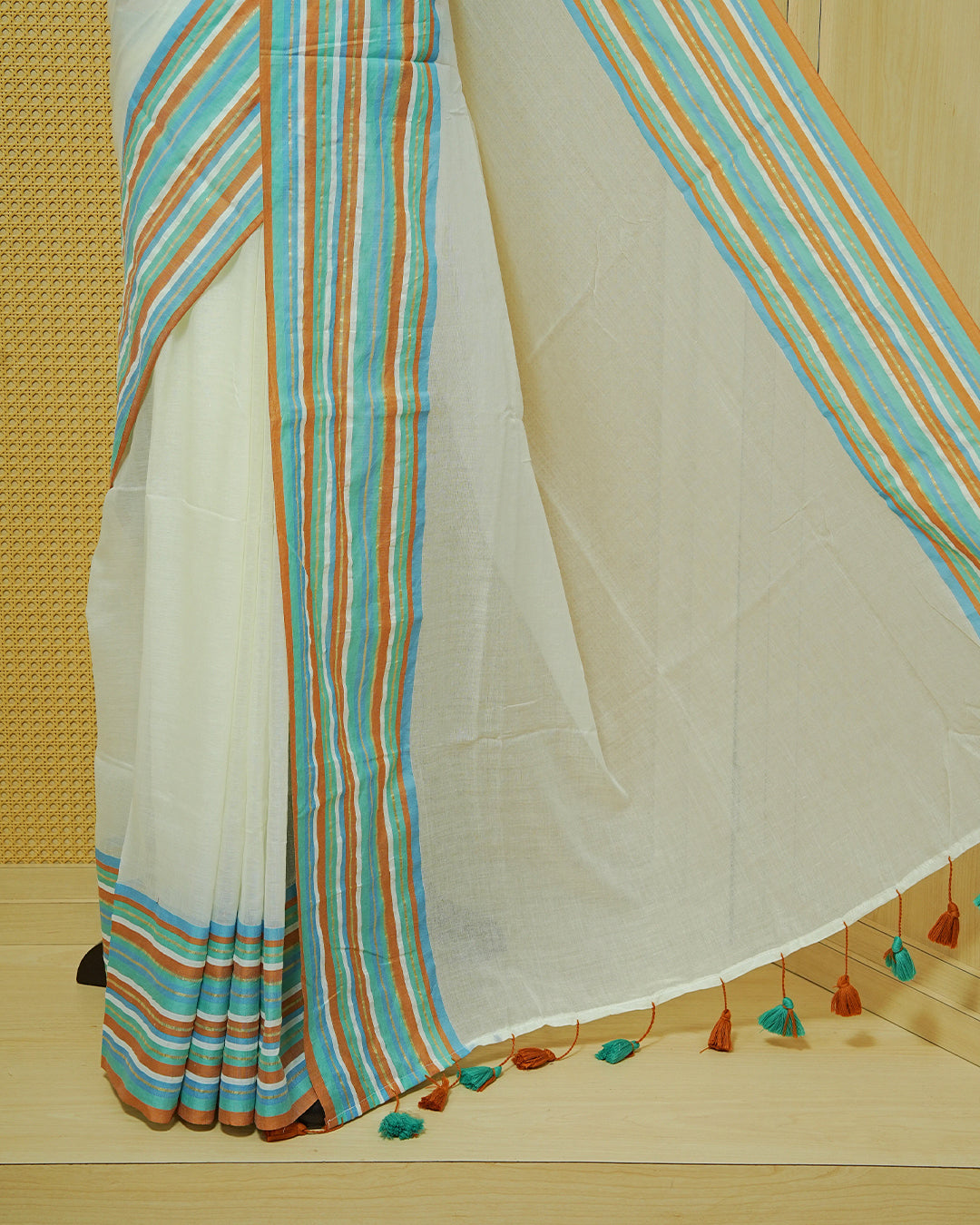 Cream colour Mul cotton saree featuring Elegant Plain body, complemented by contrast Aqua, Blue, Brown & gold zari border & Tassels.