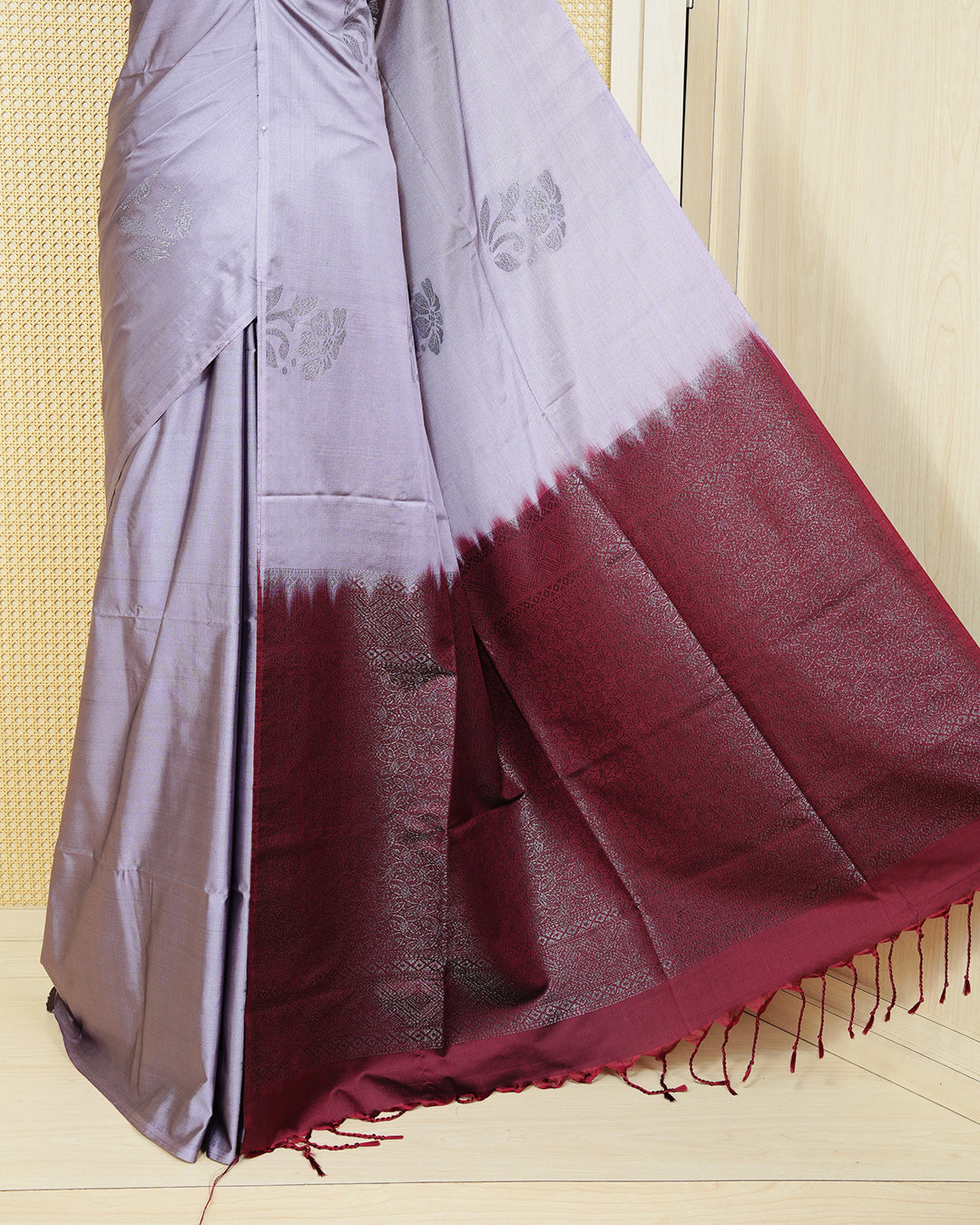 Greyish lavender colour soft silk saree featuring antique zari motifs on body with contrast dark maroon colour pallu & paired with matching blouse piece.