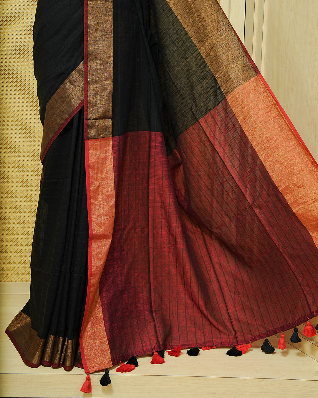 Black Colour  Mul Cotton Saree featuring an elegant plain body, complemented by a rich copper zari border and a maroon contrast pallu with red and black tassels.