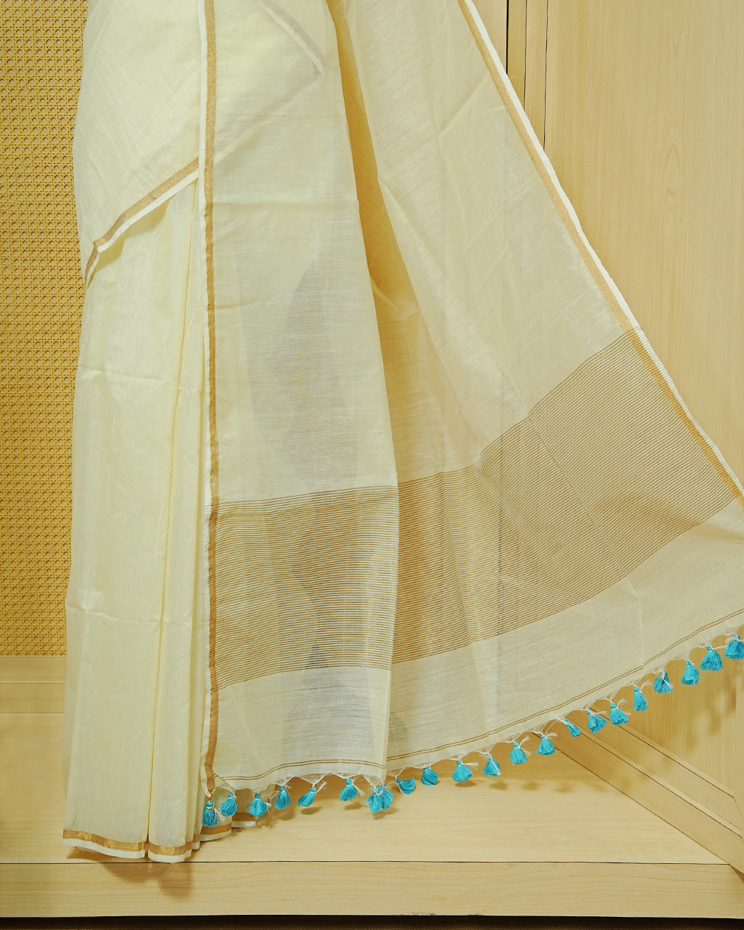 Cream Mul Cotton Saree featuring an elegant plain body, complemented by a subtle gold zari border and sky blue tassels.