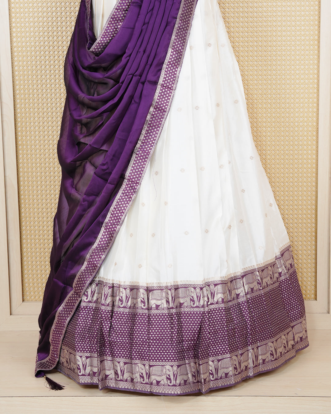 Cream coloured semi silk semi stitched dhavani set featuring gold zari buttas on the body with a contrast purple skirt with a gold zari elephant border, matching blouse piece and dupatta