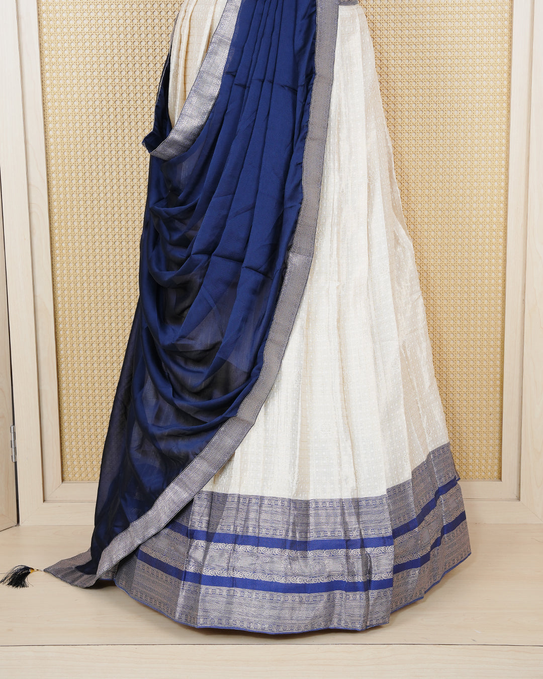 Cream colour tissue Semi stitched dhavani set featuring Gold zari check pattern with motifs on body ,contrast Blue colour with gold zari bordered skirt, paired with matching blouse piece & dupatta.