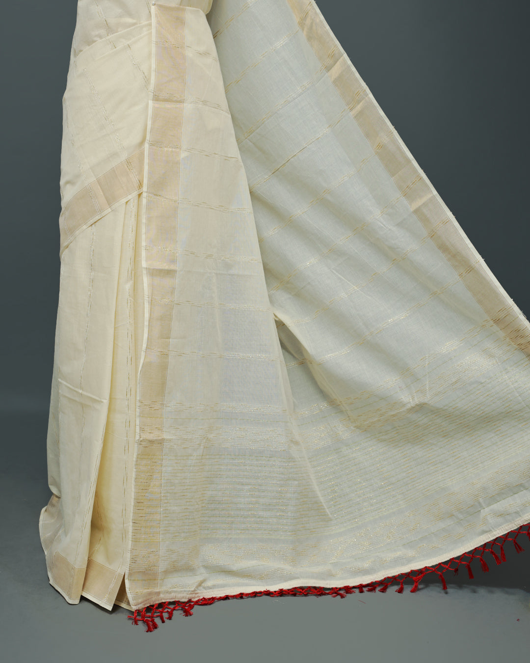 Cream colour Cotton kerala saree featuring Gold Embroidery strips on the body, complemented by a gold zari Border, red elegant tassels, paired with a matching blouse piece.