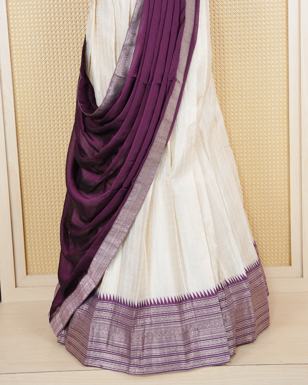 Cream colour tissue Semi stitched dhavani set featuring Gold zari check pattern with motifs on body ,contrast Purple colour with gold zari bordered skirt, paired with matching blouse piece & dupatta.