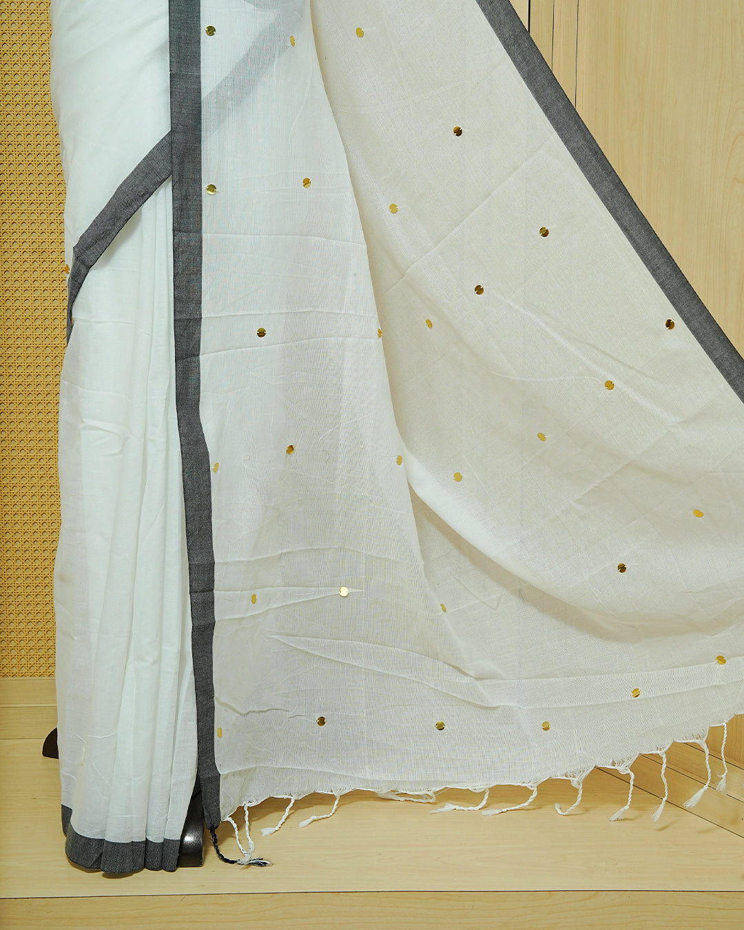 White colour Mul cotton saree featuring Gold Sequins, complemented by Contrast Black simple Border & tassels.