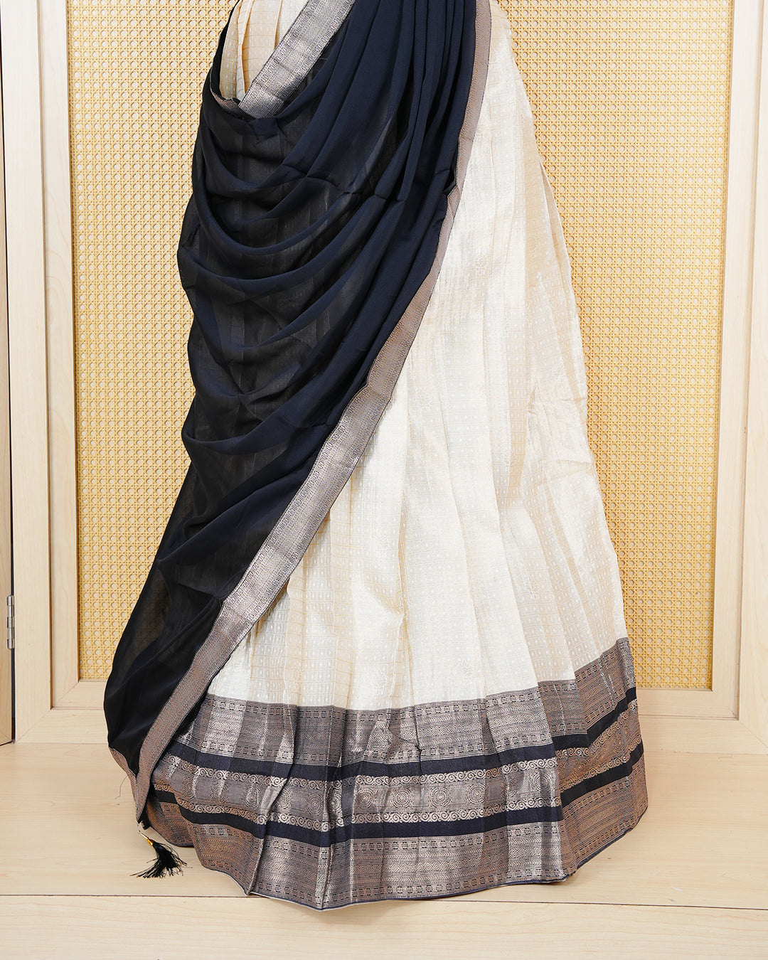 Cream colour tissue Semi stitched dhavani set featuring Gold zari check pattern with motifs on body ,contrast Black colour with gold zari bordered skirt, paired with matching blouse piece & dupatta.
