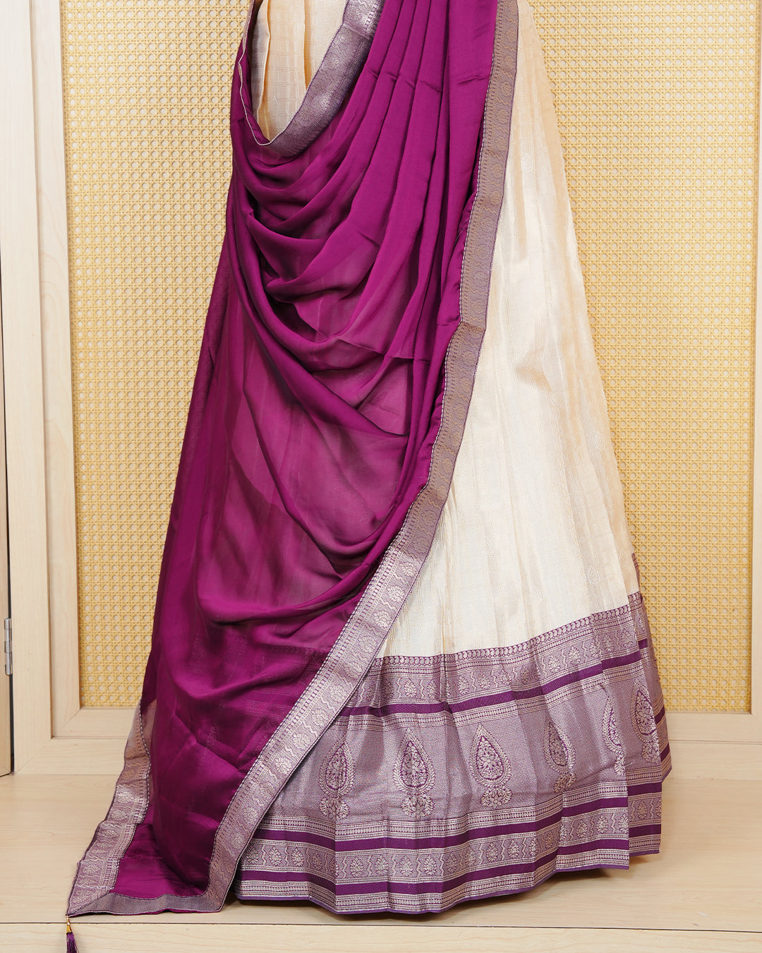 Cream colour  tissue  Semi stitched dhavani set featuring Gold zari check pattern on body ,contrast Purple colour with gold zari bordered skirt, paired with matching blouse piece & dupatta.