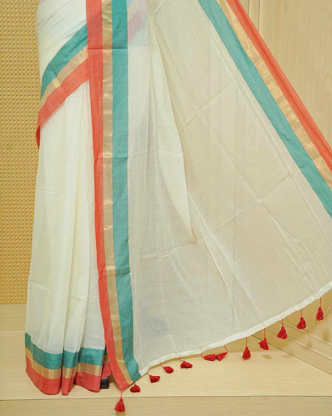 Cream colour Mul cotton saree featuring Elegant Plain body, complemented by contrast Red, Green & gold zari border & Tassels.