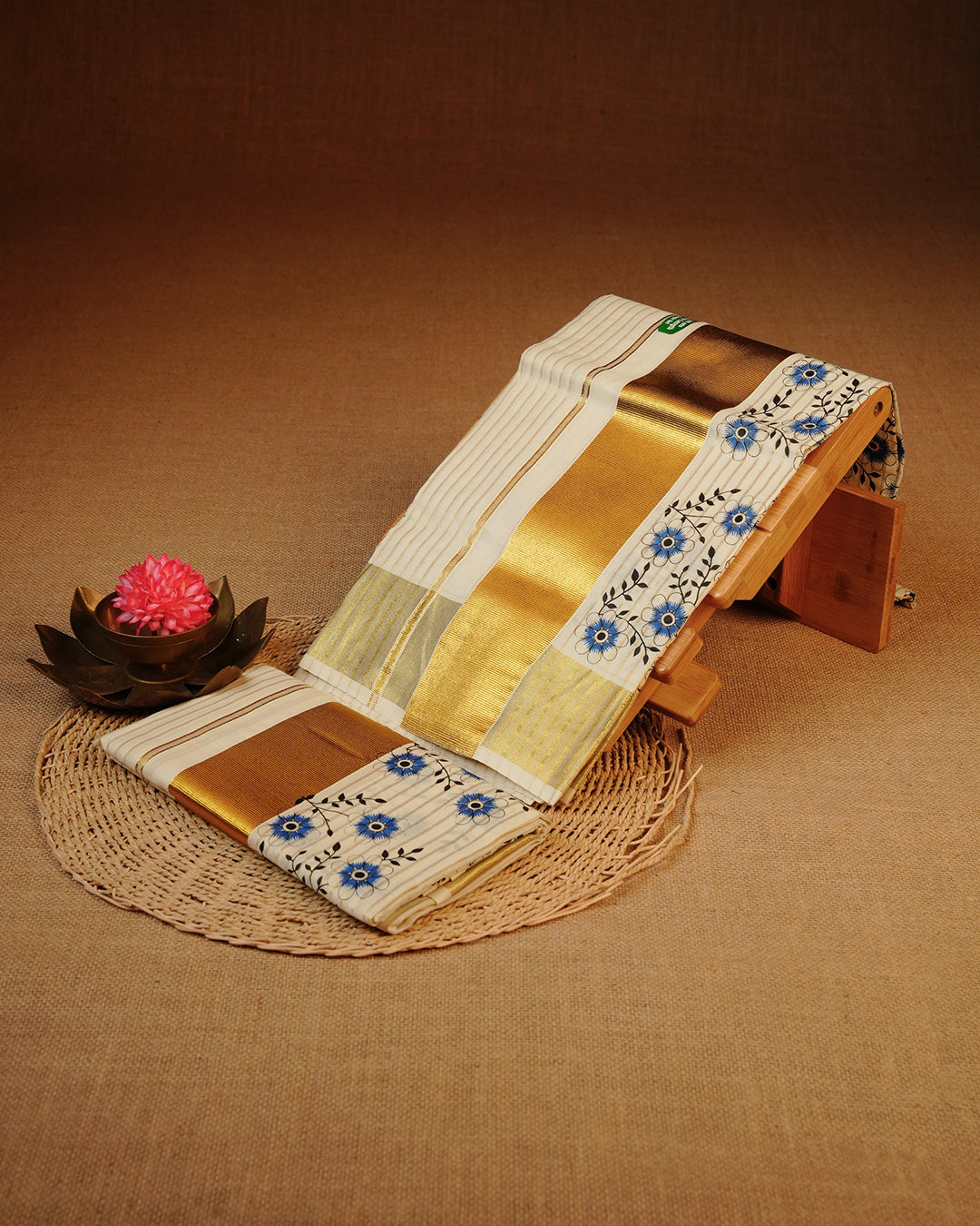 Cream colour cotton Set Mundu With Gold Zari stripes on body, enhanced with gold Kasav With Blue Floral Printed kara.