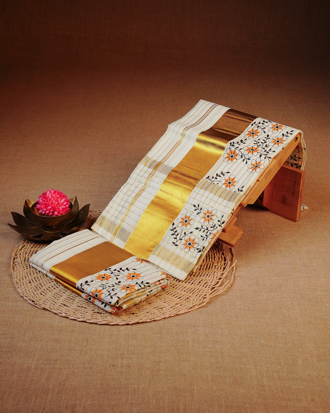 Cream colour Cotton set mundu features a Strip on body accented by a Gold with Orange Floral pattern on border.