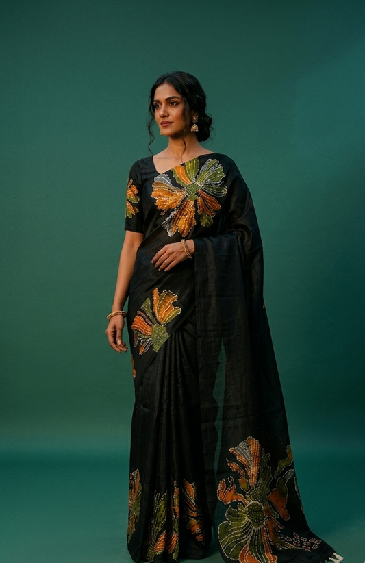 Black colour semi khadi silk saree adorned with multi colour bold floral motifs across the body, designed without a border for a contemporary touch, and paired with a matching blouse.