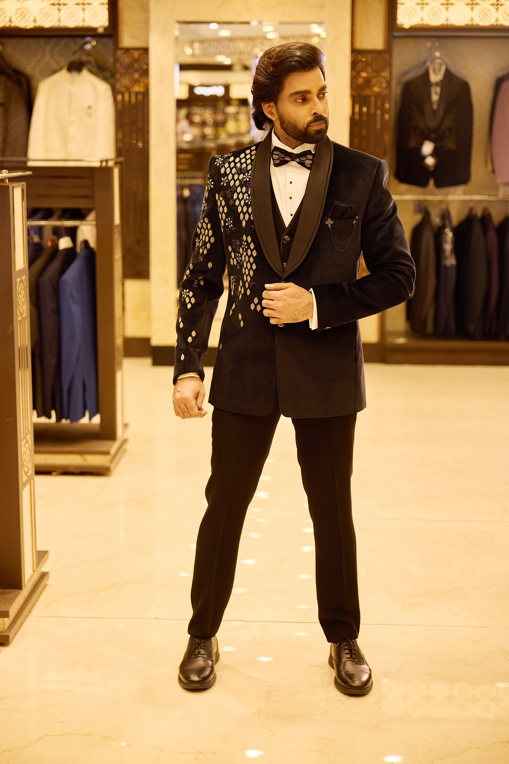 Navy blue 5 piece velvet tuxedo suit featuring an asymmetric design with gold embroidered diamond and floral patterns on one side, finished with a sleek satin lapel, double button closure, and a stylish chain and brooch detail.