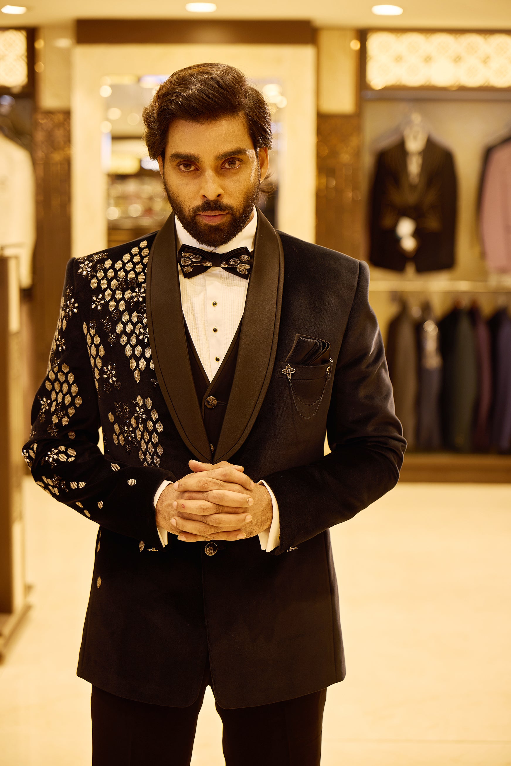 Navy blue 5 piece velvet tuxedo suit featuring an asymmetric design with gold embroidered diamond and floral patterns on one side, finished with a sleek satin lapel, double button closure, and a stylish chain and brooch detail.