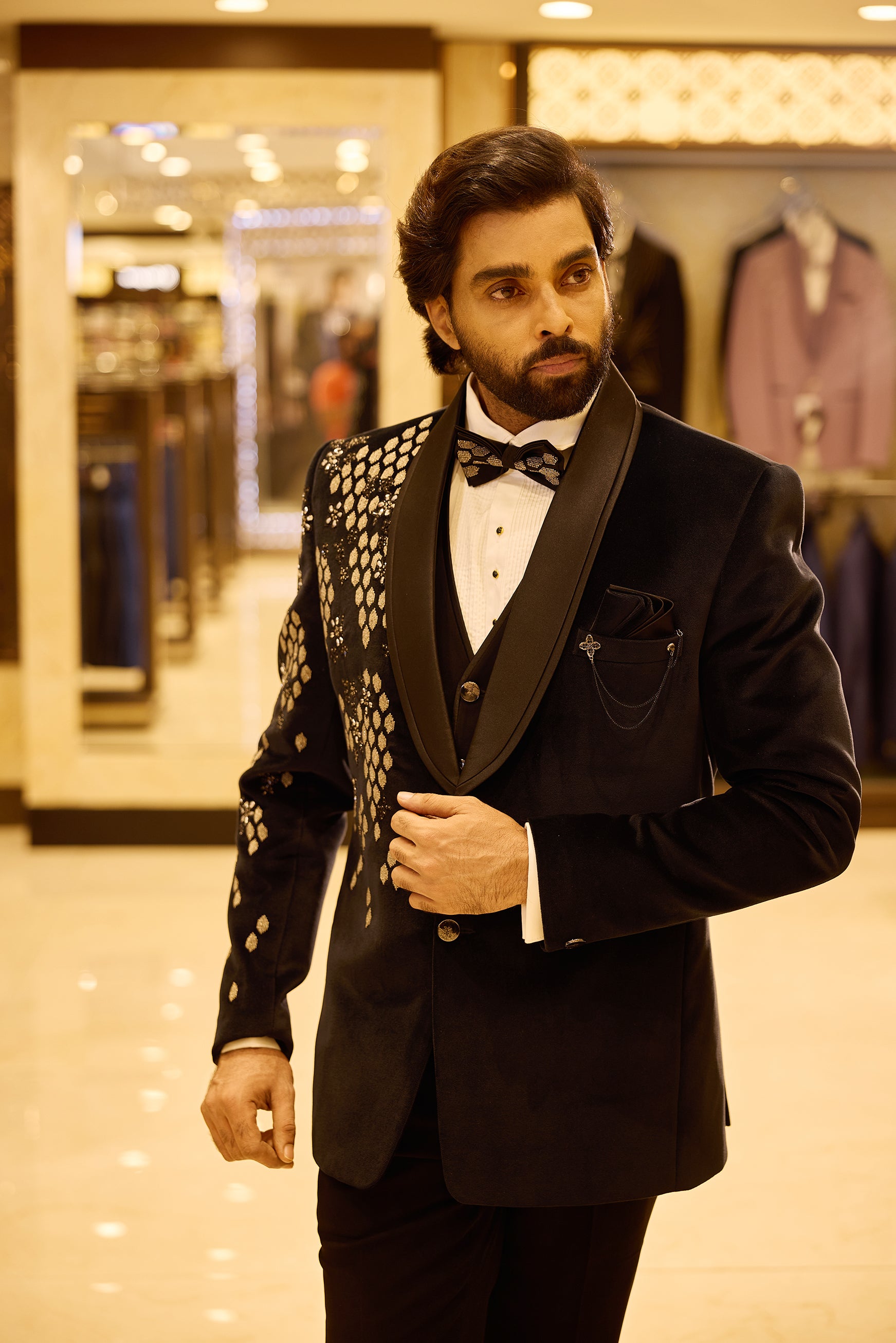 Navy blue 5 piece velvet tuxedo suit featuring an asymmetric design with gold embroidered diamond and floral patterns on one side, finished with a sleek satin lapel, double button closure, and a stylish chain and brooch detail.