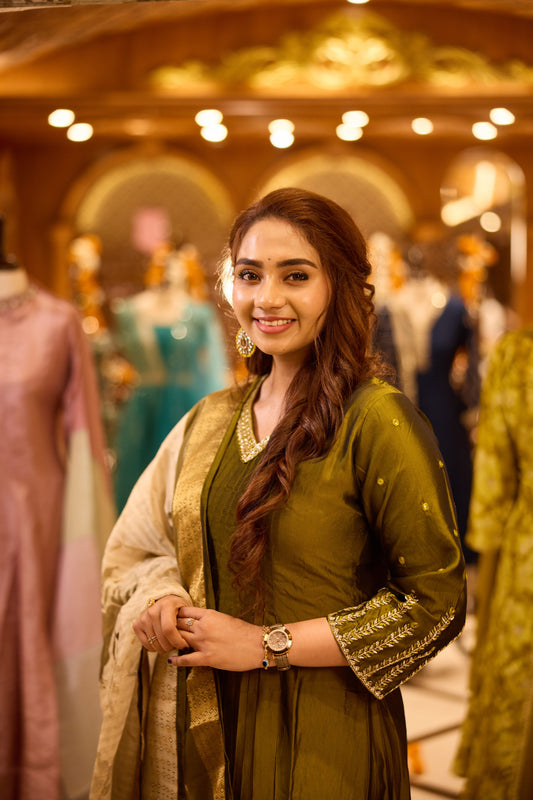Elegant olive green Anarkali suit with cut bead work on the neckline and intricate thread embroidery on sleeves. Paired with a contrasting dupatta highlighted with a zari border for a refined ethnic look.