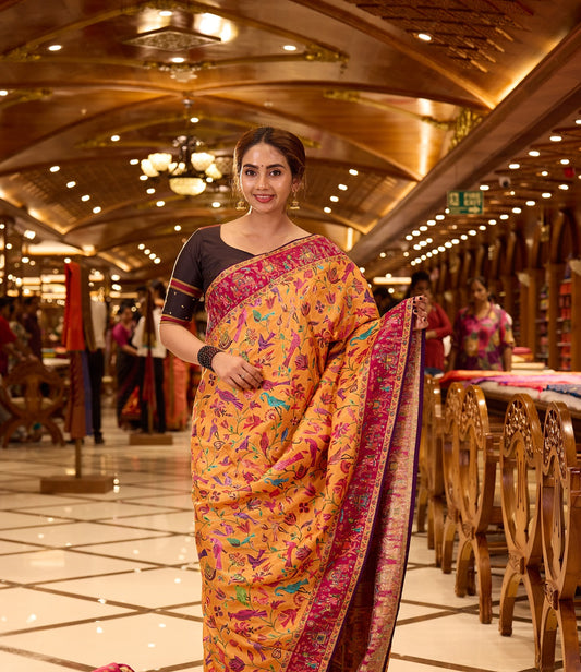Mustard Yellow Pashmina Silk saree beautifully adorned with intricate multicolor floral and bird motifs woven across the body, complemented by a contrasting maroon border and paired with a matching blouse piece.