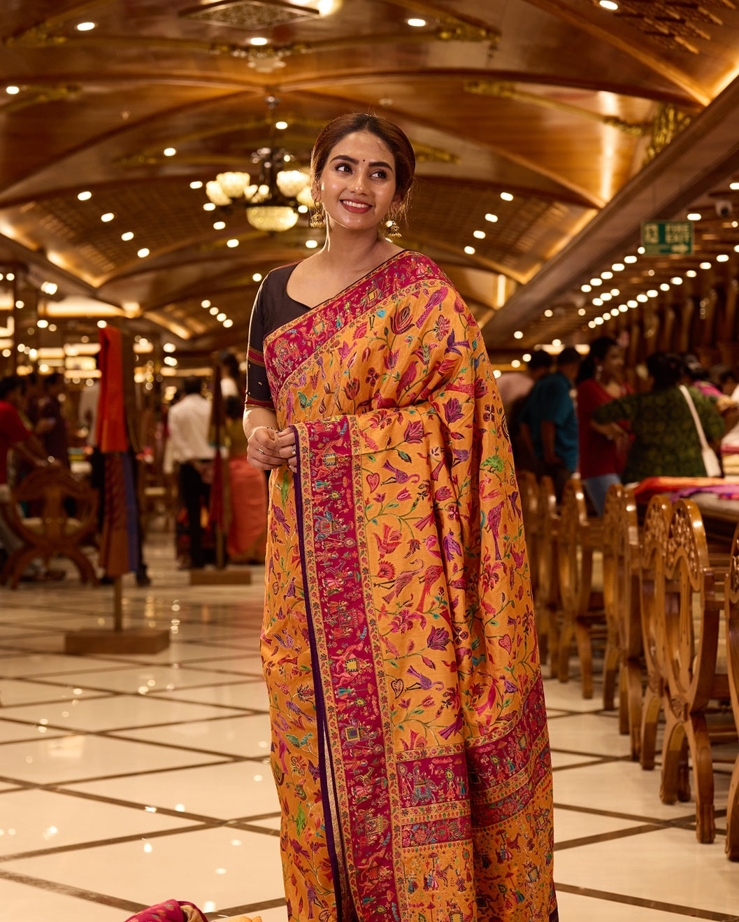 Mustard Yellow Pashmina Silk saree beautifully adorned with intricate multicolor floral and bird motifs woven across the body, complemented by a contrasting maroon border and paired with a matching blouse piece.