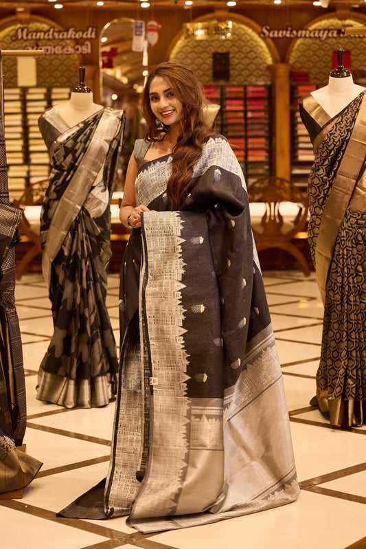 Charcoal black pure Kancheepuram silk saree with silver zari buttis, featuring a London architecture inspired silver zari pallu, a broad silver zari border, and a matching blouse
