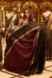 Black colour pure silk saree featuring a rich gold zari border, highlighted with a contrast deep red geometric patterned body and an elegant black pallu, beautifully paired with a matching blouse.