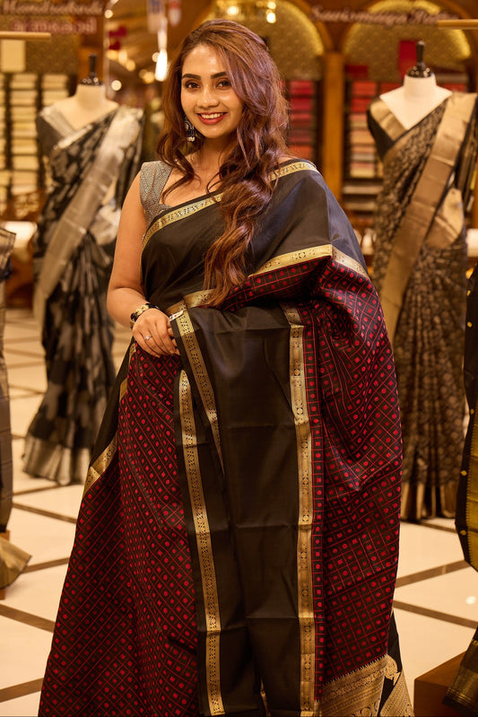 Black colour pure silk saree featuring a rich gold zari border, highlighted with a contrast deep red geometric patterned body and an elegant black pallu, beautifully paired with a matching blouse.