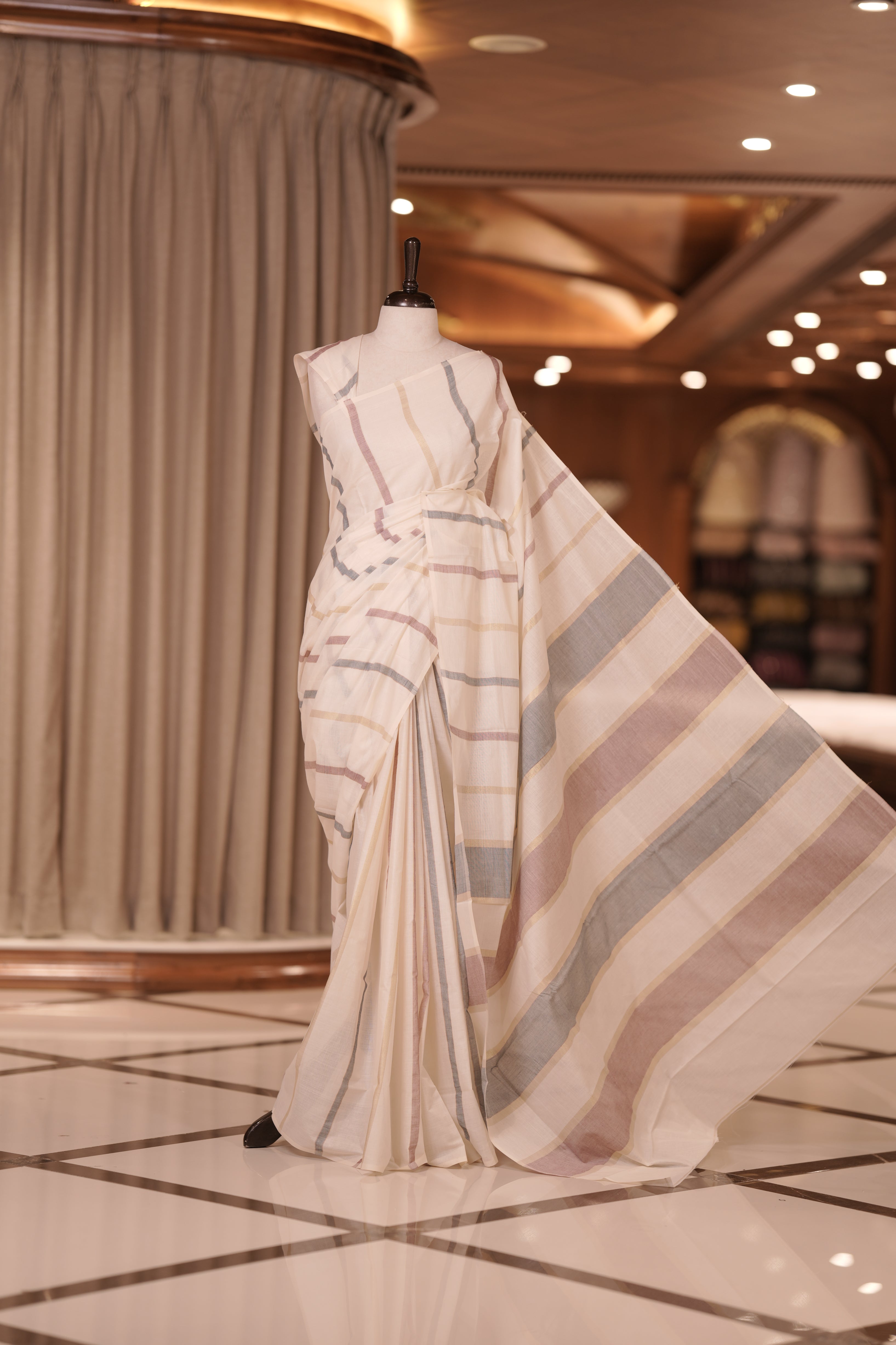 Cream colour handloom cotton saree adorned with light golden lines and a subtle maroon shade & The matching pallu enhances its timeless charm, making it perfect for graceful traditional and festive occasions.