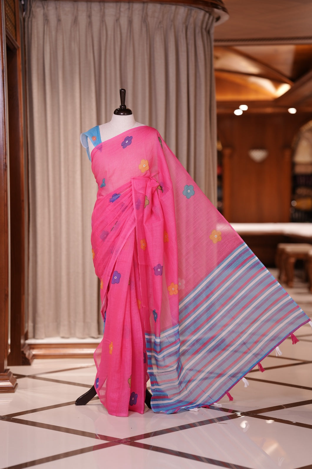 Pink colour Soft linen saree adorned with multiple floral digital prints all over, complemented by a contrast striped pallu & Paired with a beautifully contrasted printed blouse piece for an elegant contemporary look.
