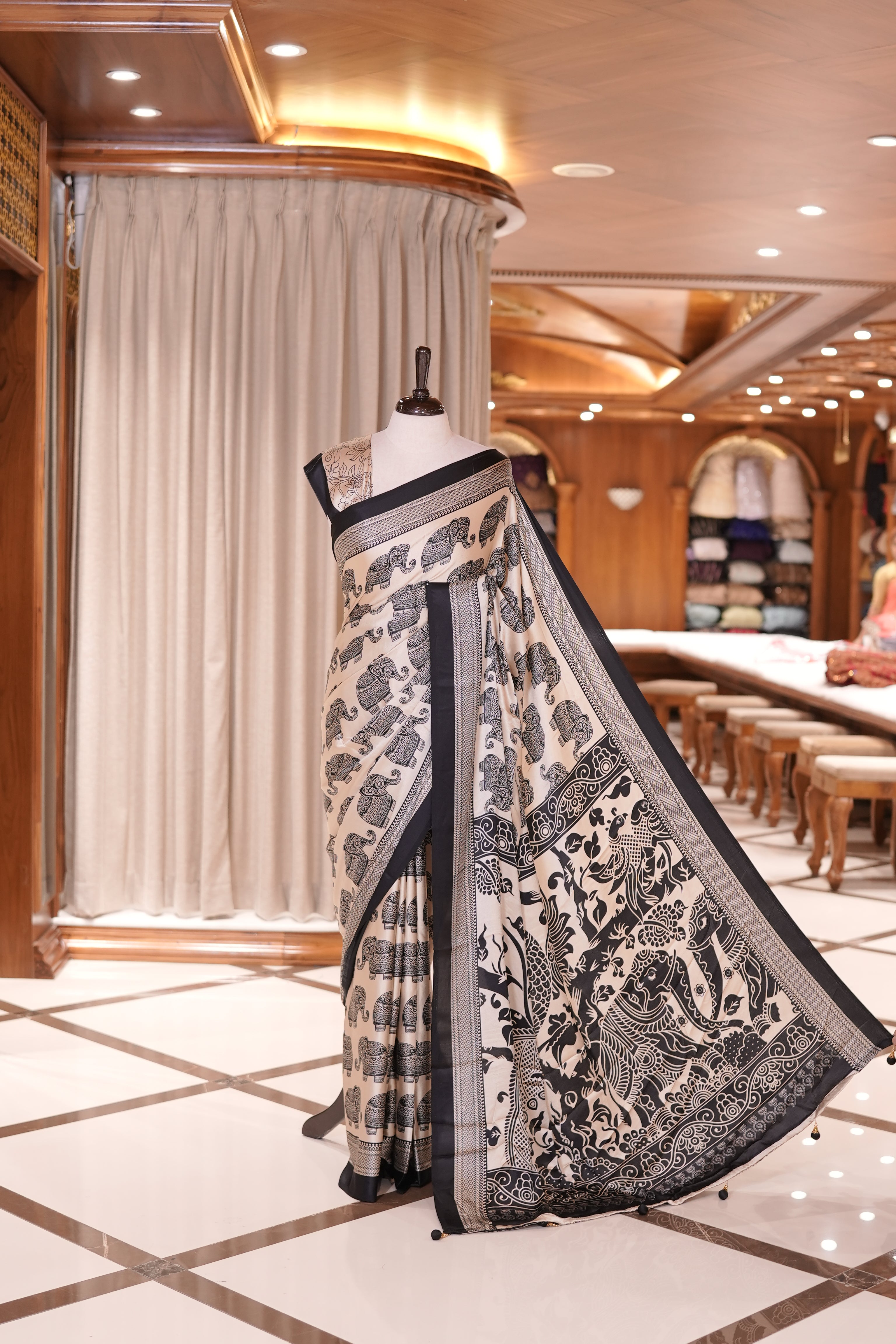 Cream and black satin modal saree featuring intricate elephant motifs and an artistic pallu, paired with a matching blouse