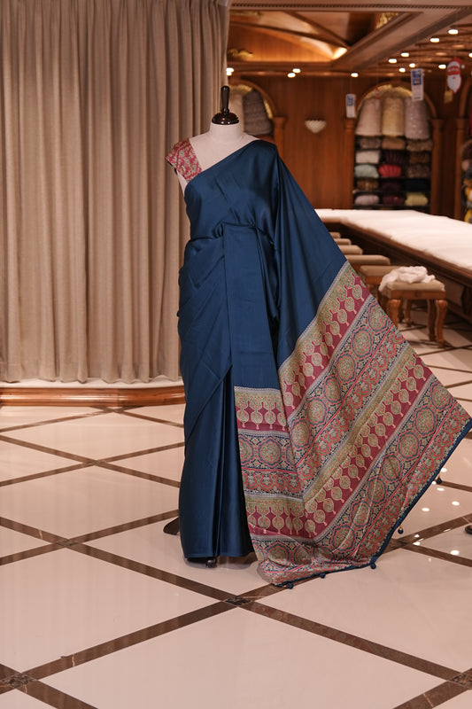 Blue Colour semi modal saree featuring a graceful solid body, beautifully enhanced with an intricately woven contrast Ajrakh printed pallu and a perfectly matching Ajrakh blouse.