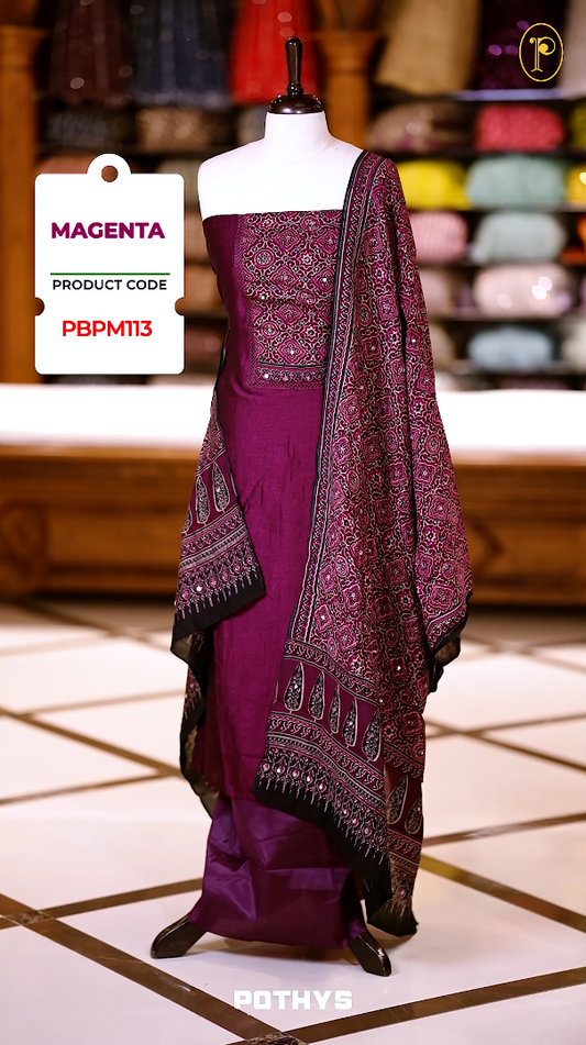 Magenta colour Ajrakh print semi silk churidhar material with intricately patterned top, mirror work highlights, printed dupatta with detailed border, and plain bottom perfect for elegant festive and casual wear.