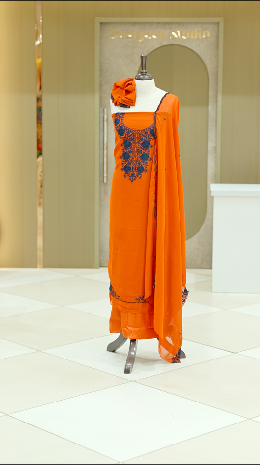 Orange colour georgette salwar suit material featuring intricate Navy Blue floral thread embroidery on the neckline and side opening, complemented with a matching bottom and dupatta. Comes with lining included for added comfort and finish.