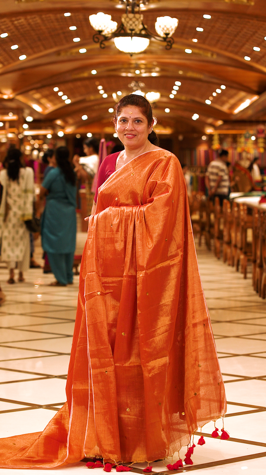 Orange colour Semi Tissue saree featuring a plain body adorned with delicate sequin detailing throughout, crafted in a borderless design. Comes without a blouse piece.
