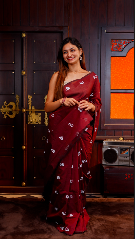 Maroon colour Poly cotton saree featuring Malayalam Letters Print on body, pallu with tassels, Contrast Colour Blouse piece.