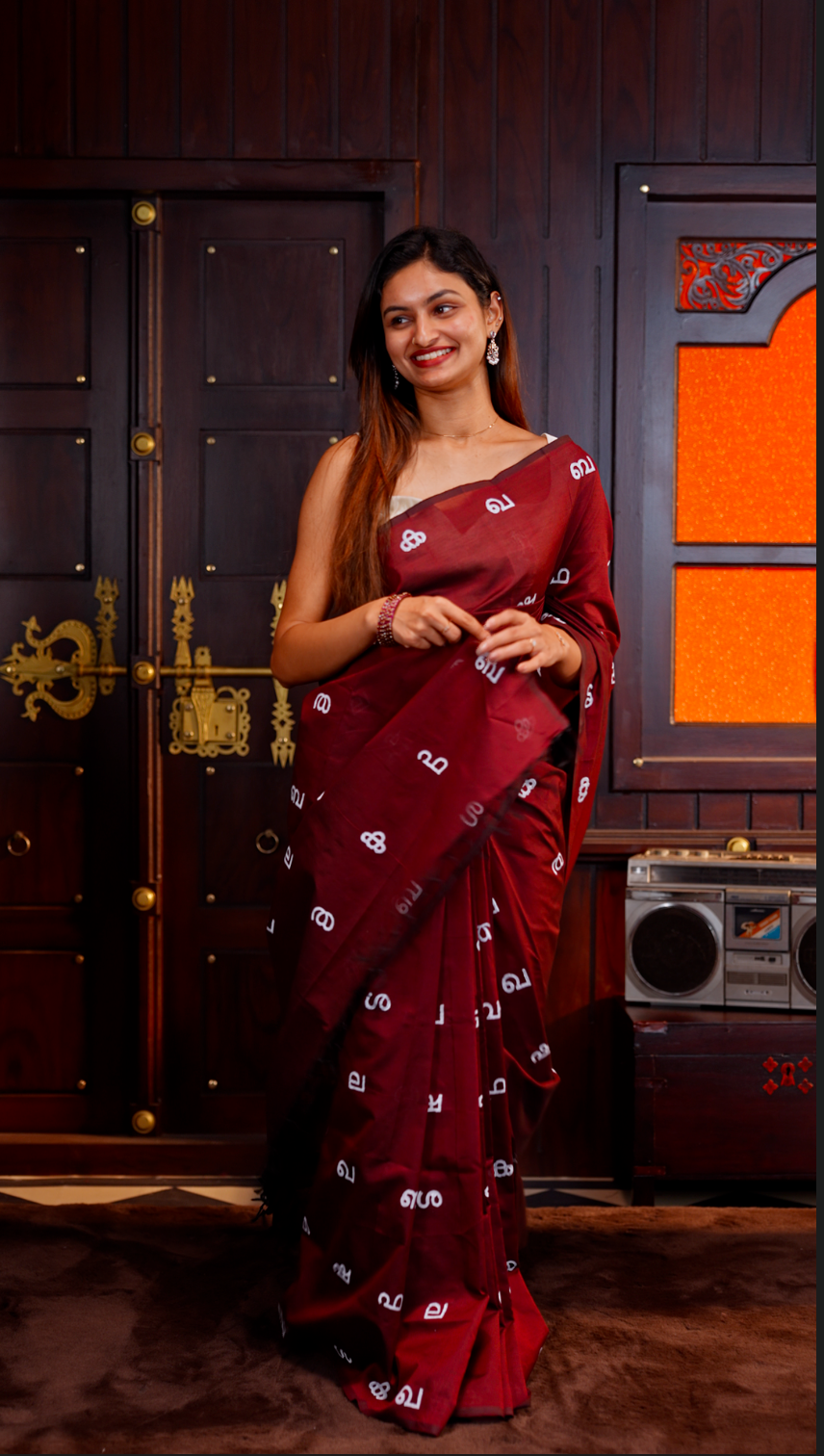 Maroon colour Poly cotton saree featuring Malayalam Letters Print on body, pallu with tassels, Contrast Colour Blouse piece.