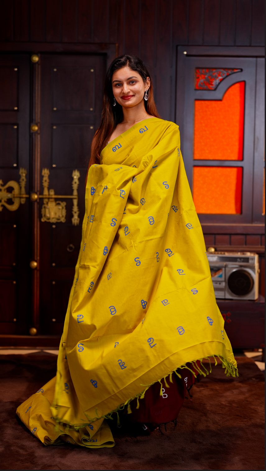Olive Yellow colour Poly cotton saree featuring Malayalam Letters Print on body, pallu with tassels, Contrast Colour Blouse piece.