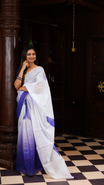 White colour linen saree featuring Blue colour small floral print on body, complemented by contrast Colour border, big floral print & tassels on pallu, comes with contrast colour blouse piece.