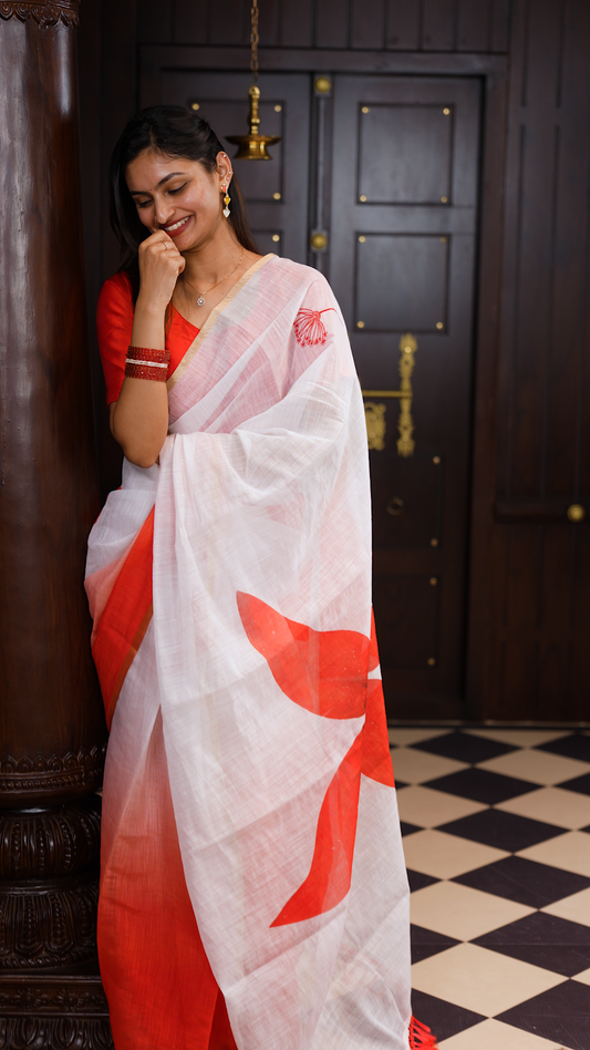 White colour linen saree featuring Red colour small floral print on body, complemented by contrast Colour border, big floral print & tassels on pallu, comes with contrast colour blouse piece.