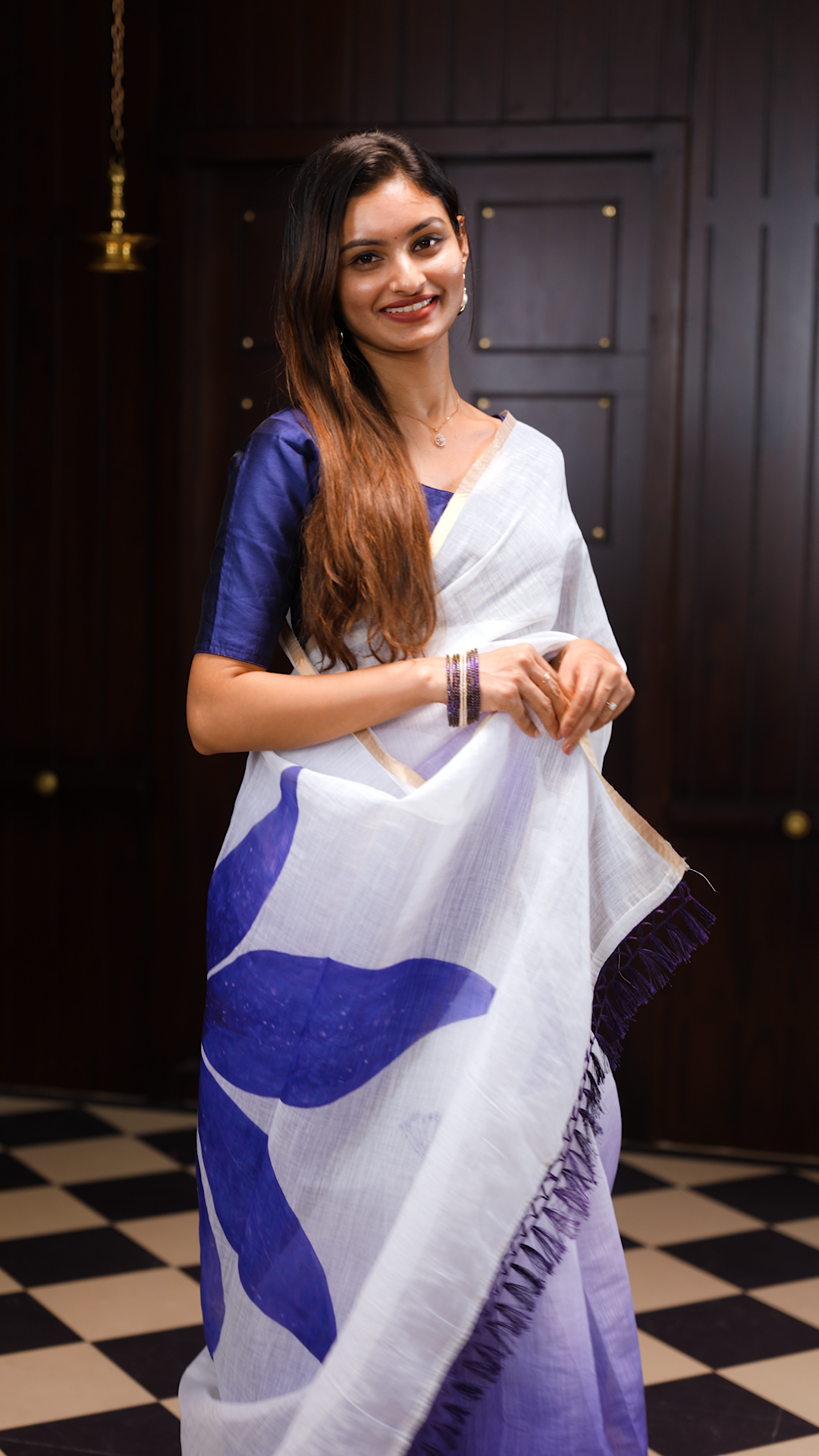 White colour linen saree featuring Blue colour small floral print on body, complemented by contrast Colour border, big floral print & tassels on pallu, comes with contrast colour blouse piece.