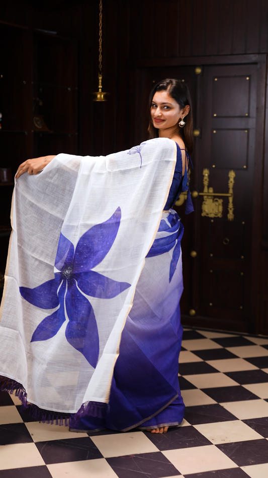 White colour linen saree featuring Blue colour small floral print on body, complemented by contrast Colour border, big floral print & tassels on pallu, comes with contrast colour blouse piece.