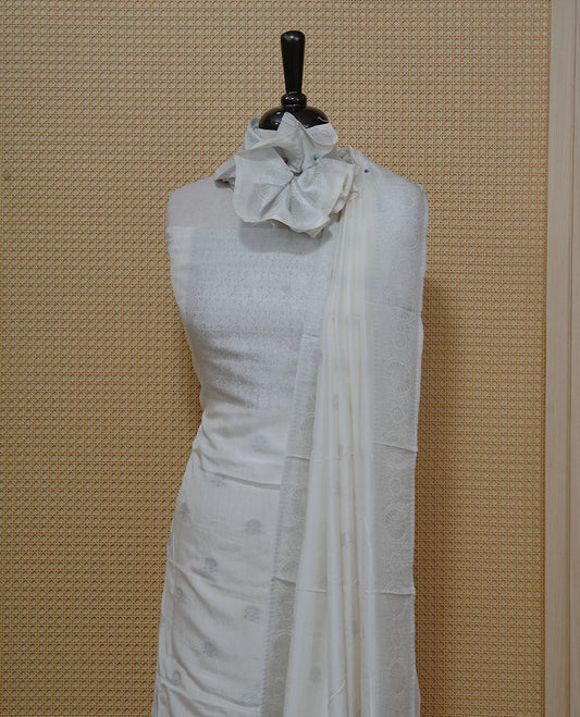 Cream colour Salwar material featuring silver zari Buttas on body & zari worked Neck Portion, paired with matching dupatta & Bottom.