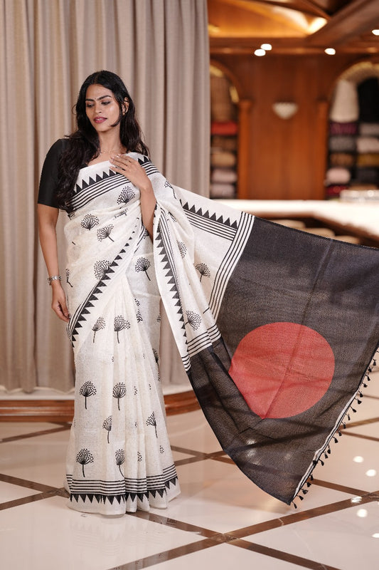 White colour semi khadi saree adorned with black floral motifs and a striking red circle pallu, exuding timeless elegance and contemporary charm & Comes with a matching blouse piece.