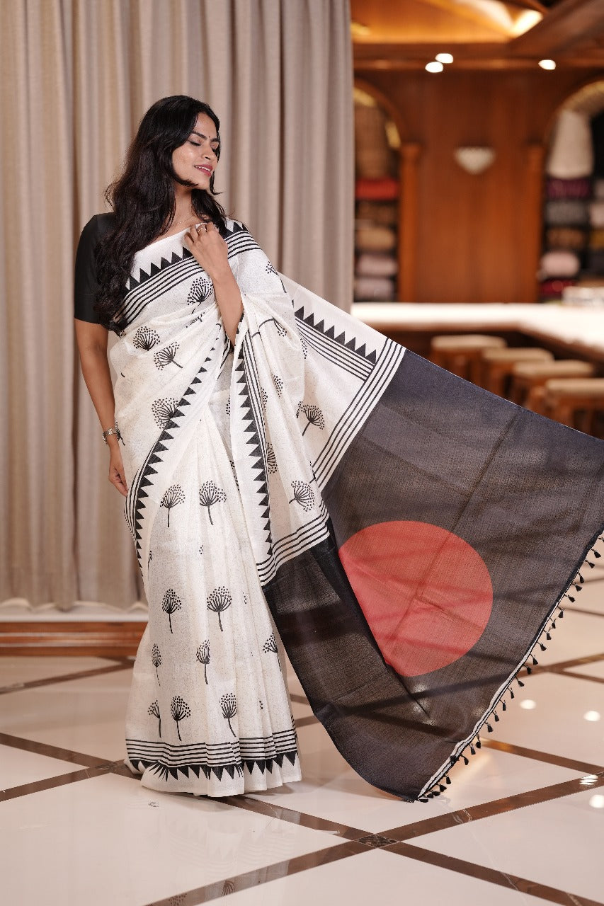White colour semi khadi saree adorned with black floral motifs and a striking red circle pallu, exuding timeless elegance and contemporary charm & Comes with a matching blouse piece.