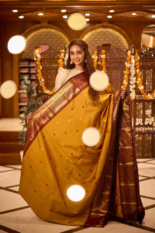 Pure silk saree featuring a mustard yellow body adorned with small zari and thread motifs, complemented by a rich maroon zari woven border and grand pallu.