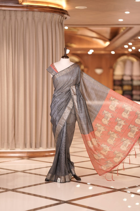 Ash & peach colour Dolla silk saree featuring a striped body with a matching golden zari border, The pallu showcases exquisite Kalamkari prints, complemented by a contrast printed blouse.