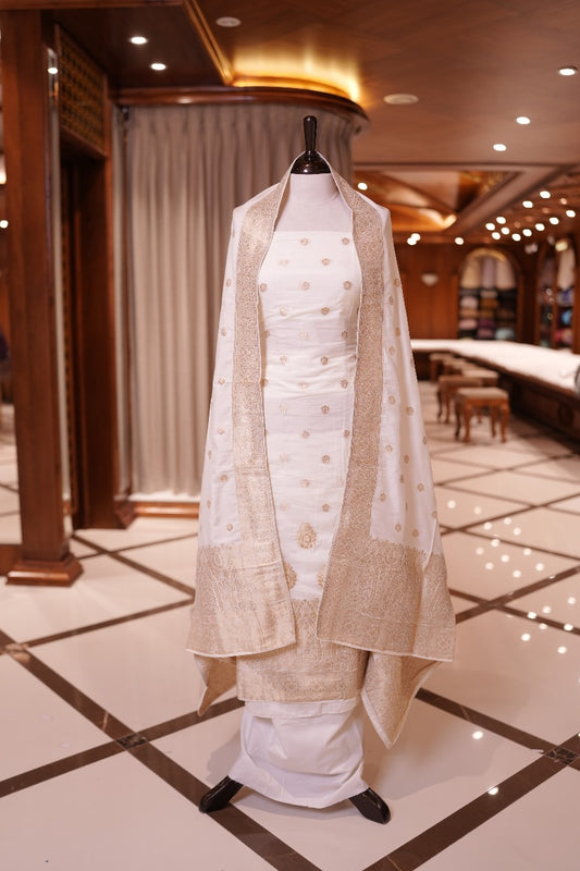 White colour Semi Banarasi Silk top adorned with elegant gold zari floral motifs and a rich border, paired with a zari worked dupatta and a plain bottom.