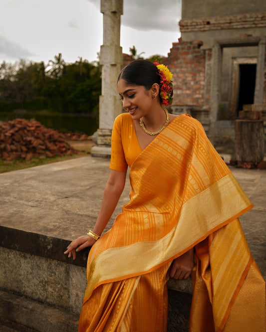 Golden mustard colour Samudrika wedding saree featuring elegant vertical geometric jacquard designs woven in antique silver and copper zari, complemented by a traditional zari pettu border and paired with a matching blouse piece.