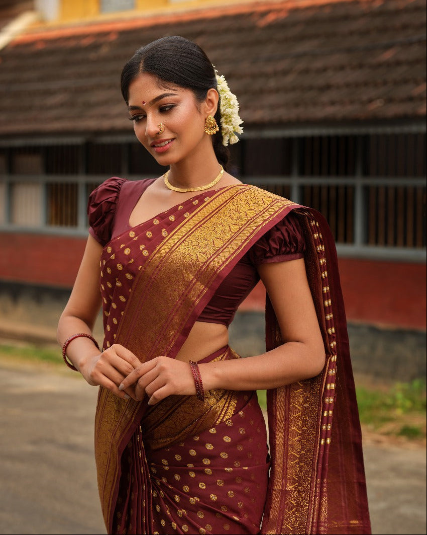 Dark brown colour Samudrika Pattu saree featuring traditional round motifs with antique silver zari Meenakari weaving across the body, beautifully complemented by a classic heritage gold zari border and paired with a matching blouse piece.