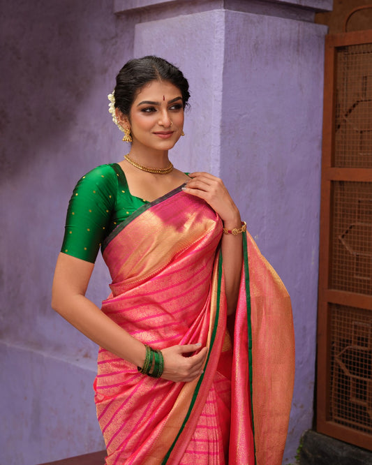 Rani pink colour Samudrika Pattu saree featuring elegant horizontal zari jacquard weaving, complemented by a traditional gold zari border accentuated with green piping for a striking finish, and paired with a matching blouse piece.