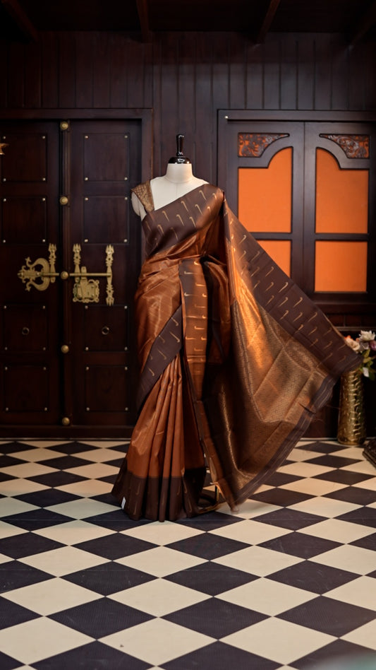 Copper colour Kanchi silk saree featuring a contrast border with Zari motifs and elegant Vertical weaving design across the body, beautifully paired with a matching blouse.
