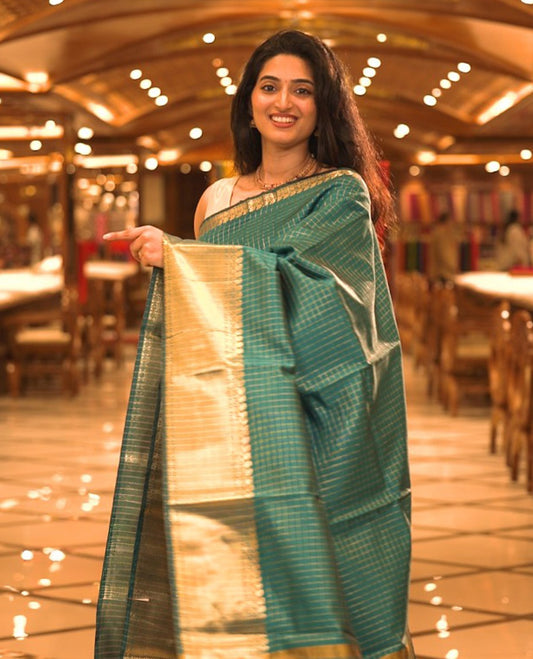 Peacock Blue colour semi banaras lichi silk saree featuring checked patterned body, complemented by gold zari border, paired with matching blouse piece.