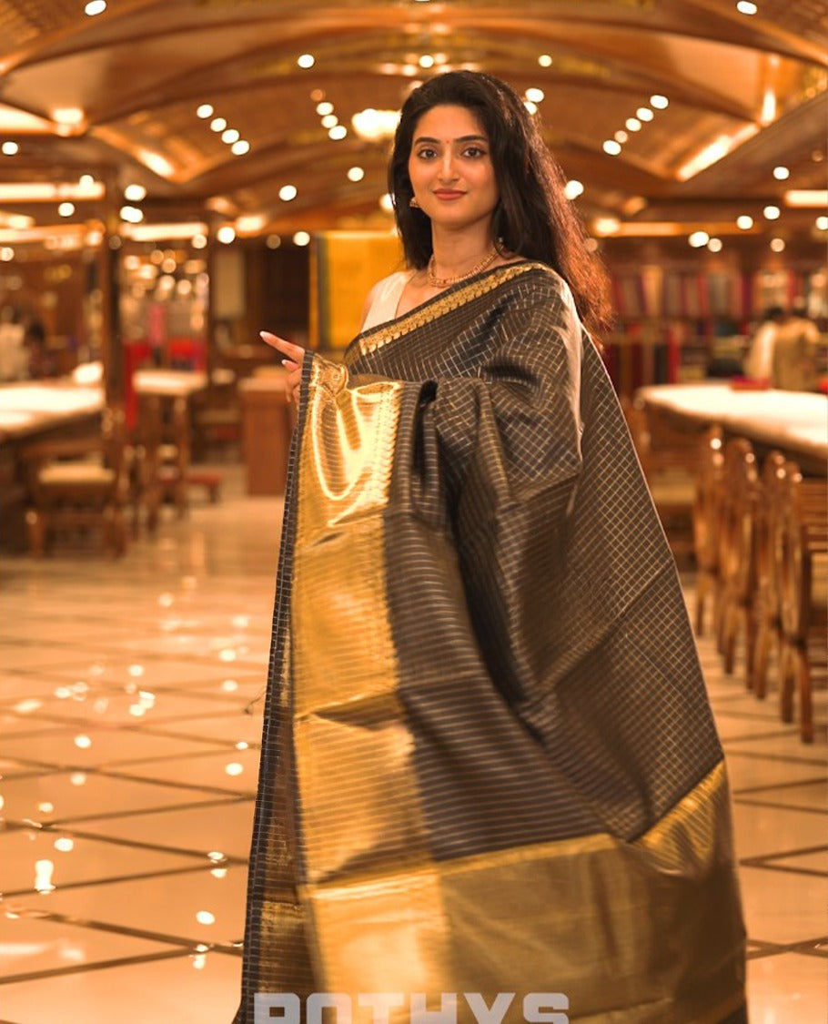 Black colour semi banaras lichi silk saree featuring checked patterned body, complemented by gold zari border, paired with matching blouse piece.